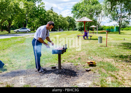 Di Zrenjanin, Vojvodina, Serbia - Giugno 24, 2018: l uomo è simmering carni macinate su barbecue grill, griglia in metallo a escursione tradizionale sito. Foto Stock