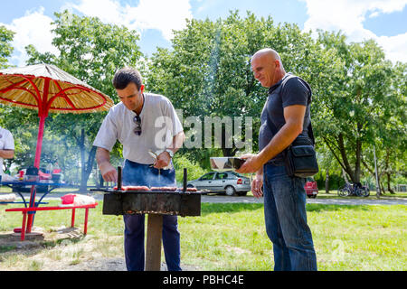 Di Zrenjanin, Vojvodina, Serbia - Giugno 24, 2018: uomo estrarre spiedini arrosto con pinze in metallo, li rimuove da barbecue in contenitore di plastica. Foto Stock