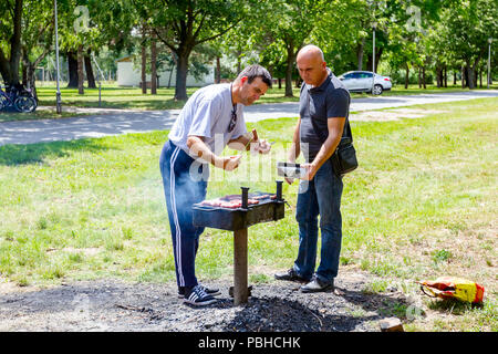 Di Zrenjanin, Vojvodina, Serbia - Giugno 24, 2018: uomo estrarre spiedini arrosto con pinze in metallo, li rimuove da barbecue in contenitore di plastica. Foto Stock