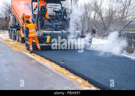 Lavoratore di asfalto operativo lastricatore macchina durante la costruzione di strade e lavori di riparazione. Foto Stock