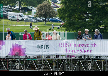 Visitatori Showground ad RHS Chatsworth Flower Show, in piedi dal banner promozionali & guardando sopra, temporanea river bridge - Derbyshire, Inghilterra, Regno Unito. Foto Stock