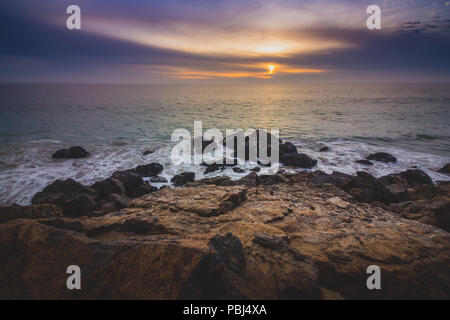 Drammatico il cielo al tramonto lungo Point Dume membro spiaggia con onde che si infrangono in formazioni rocciose lungo la spiaggia, Malibu, California Foto Stock