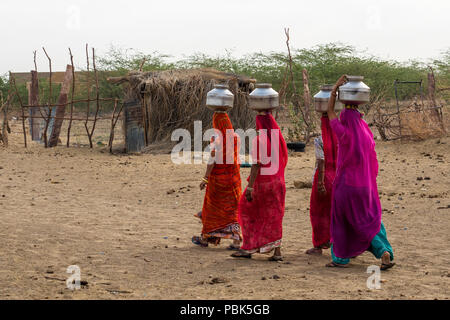 Le donne delle zone rurali portano caraffe di metallo con acqua sulle loro teste. Deserto Parco Nazionale di Jaisalmer India Giugno 2018 Foto Stock