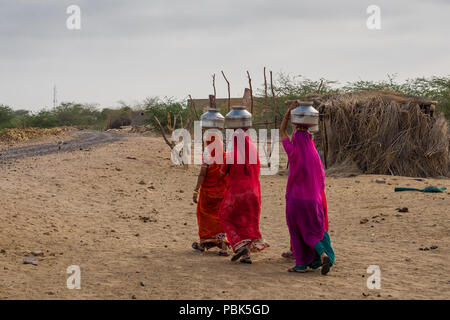 Le donne delle zone rurali portano caraffe di metallo con acqua sulle loro teste. Deserto Parco Nazionale di Jaisalmer India Giugno 2018 Foto Stock