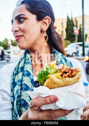 Athens, Grecia - 29 giugno 2018. Donna greca di mangiare un tradizionale di autogiro, impostato su pane pita, tipico del greco cibo di strada. Foto Stock