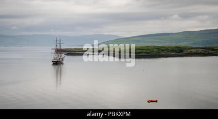 A Tall Ship è ancorata nell'acciaio-acque grigie di Tobermory Bay sull'Isola di Mull tra le montagne di West Highlands della Scozia. Foto Stock