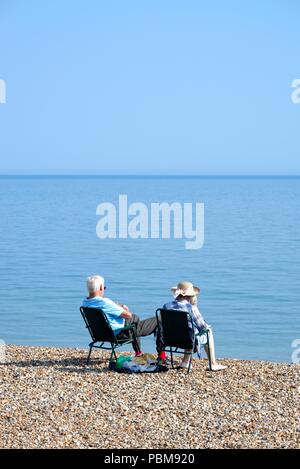 Anziana coppia bianco seduto sulla spiaggia a Hastings in una calda giornata estiva, East Sussex England Regno Unito Foto Stock