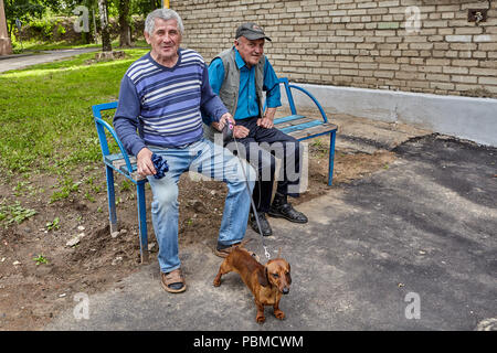 Vitebsk, Bielorussia - Luglio 7, 2018: due anziani uomini bielorussi sedersi sulla panchina nel parco, uno di essi detiene bassotto al guinzaglio. Foto Stock