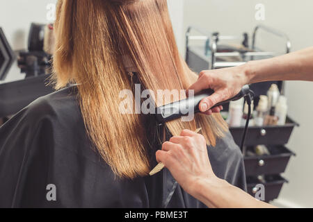 Stiratura in un salone di bellezza. Parrucchiere facendo un'acconciatura per client con un ferro da stiro per capelli Foto Stock