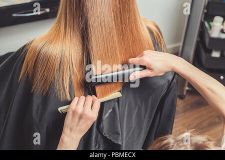 Stiratura in un salone di bellezza. Parrucchiere facendo un'acconciatura per client con un ferro da stiro per capelli Foto Stock