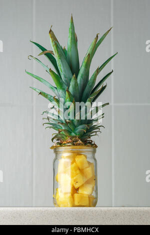 Fresh succoso e pezzi di ananas in un vasetto di vetro sul tavolo di cucina contro il grigio Sfondo piastrelle Foto Stock