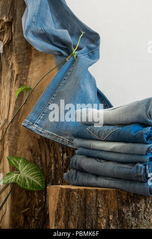 Paia di jeans appeso su un vecchio tronco di legno, sfondo bianco con spazio di copia Foto Stock