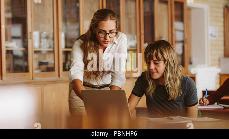 Il professor femminile aiutando uno degli studenti a lezione. Insegnante assistere il problema di uno studente nella sua classe. Foto Stock