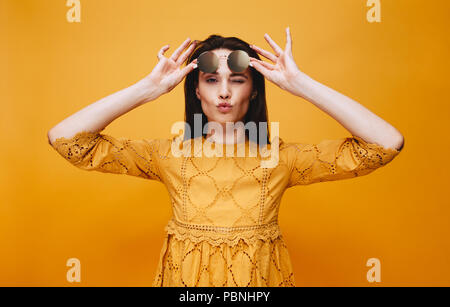 Ritratto di donna che indossa abiti di colore arancione tenendo gli occhiali da sole sul fronte, winking e soffiando un bacio. Moda modello femminile in posa con labbra rugose Foto Stock