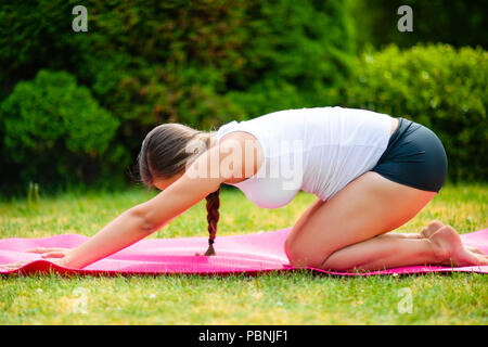Vista laterale di montare la giovane donna in stato di gravidanza la pratica del bambino sul materassino yoga in posizione di parcheggio Foto Stock