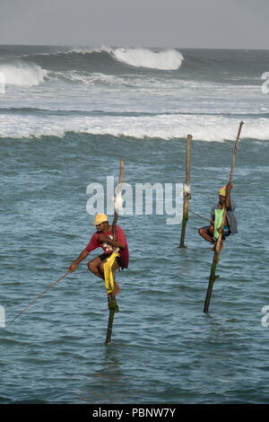 Il governo dello Sri Lanka stilt pescatori di mattina presto, pesca con grandi surf in background in Ahangama beach Foto Stock