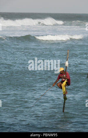 Il governo dello Sri Lanka stilt fisherman di mattina presto, pesca con grandi surf in background in Ahangama beach Foto Stock