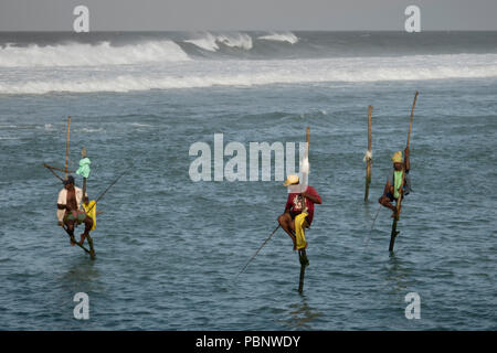 Il governo dello Sri Lanka stilt pescatori di mattina presto, pesca con grandi surf in background in Ahangama beach Foto Stock