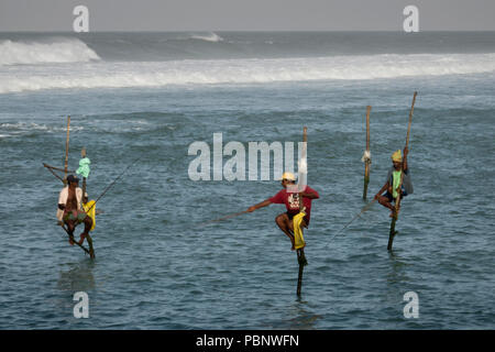 Il governo dello Sri Lanka stilt pescatori di mattina presto, pesca con grandi surf in background in Ahangama beach Foto Stock