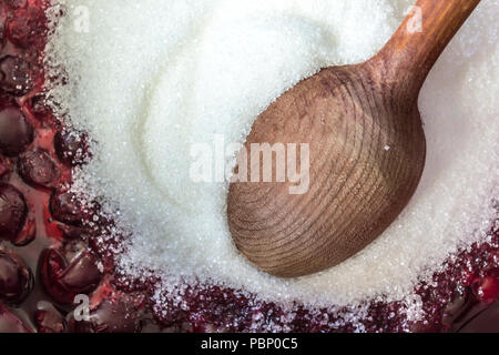 La cottura di confettura di ciliegie . Hot rosso scuro ciliegie, lo zucchero cristallizzato bianco e un cucchiaio di legno. Il sito di frutti, bacche, cibo, cucina e cottura. Foto Stock