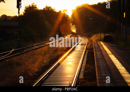 Nel tardo pomeriggio la luce del sole si riflette dal treno tracce accanto alla piattaforma presso la piccola stazione ferroviaria di quelle, vicino a Halle Westfalen (Germania). Foto Stock