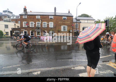 Londra REGNO UNITO. Il 29 luglio 2018. Spettatore con un grande ombrellone orologi come ciclisti passa attraverso Wimbledon Village nel Prudential Londra Surrey 100 evento classico in condizioni umide come le piogge iniziano a venire verso il basso. Il prudenziale Ride London-Surrey 100 nel suo sesto anno celebra il retaggio per il ciclismo creato dal London 2012 Giochi Olimpici e Paraolimpici e segue un 100-miglio percorso su strade chiuse attraverso la capitale e nella campagna del Surrey Credito: amer ghazzal/Alamy Live News Foto Stock