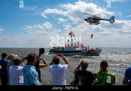 Wilhelmshaven, Germania. 29 Luglio, 2018. Ai visitatori la visione di una missione di addestramento del personale di salvataggio, durante la quale un uomo appeso a una fune viene abbassata da un elicottero sul rescue cruiser Hannes Glogner, durante il giorno della Società tedesca per il salvataggio dei naufraghi (DGzRS) presso la baia di Jadebusen. Credito: Mohssen Assanimoghaddam/dpa/Alamy Live News Foto Stock