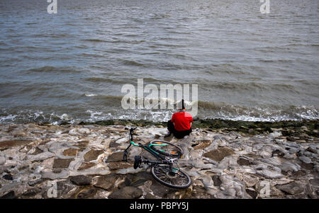 Wilhelmshaven, Germania. 29 Luglio, 2018. Una donna si siede con le cuffie sulla spiaggia a sud sul mare del Nord. Credito: Mohssen Assanimoghaddam/dpa/Alamy Live News Foto Stock