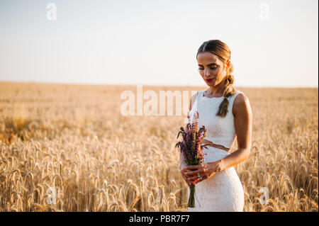 Sposa tiro con un mazzo di fiori in un campo Foto Stock