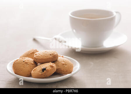 Il caffè. Porcellana Bianca tazza di caffè appena fatto top view close-up disposti con biscotti, cucchiaio e piastra su sfondo chiaro Foto Stock