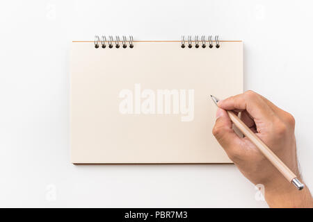 Concetto di Design - vista superiore della spirale kraft notebook, pagina vuota e mano d'uomo tenendo la penna in legno isolato su sfondo bianco per mockup Foto Stock