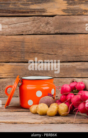 Enamelware Cup e verdure ancora in vita. Scrivania in legno sfondo. Foto Stock