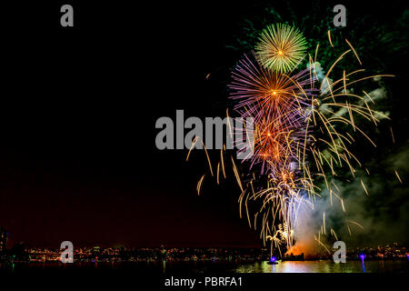 Multi Colore luci di fuochi d'artificio sull'oceano in una grande città, antico ponte e moderni edifici sullo sfondo, incandescente e di riflessione del paglierino Foto Stock