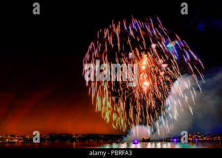 Multi colore luci di fuochi d'artificio sull'oceano in una grande città, antico ponte e moderni edifici sullo sfondo, incandescente e di riflessione del paglierino Foto Stock