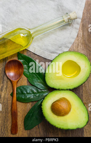 Tagliate a fette di avocado con foglie di avocado e olio di avocado in una bottiglia su un sfondo di legno Foto Stock