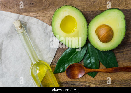 Avocado a fettine e foglie di avocado e olio di avocado in una bottiglia su un sfondo di legno Foto Stock