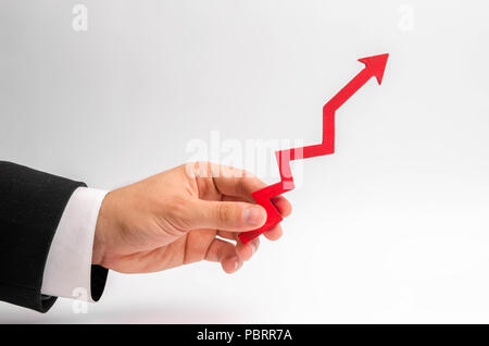 Un imprenditore il mano trattiene una freccia rossa su uno sfondo bianco. Il concetto di alzare e moltiplicando il reddito e i profitti, l'aumento dei prezzi e dei salari Foto Stock