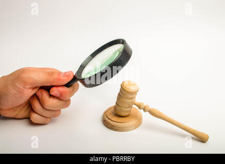 La mano con la lente di ingrandimento sguardi intensamente il martello del giudice. Il concetto di indagine della Corte casi. La corruzione nei tribunali. Un Foto Stock