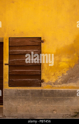 Abstract dettagli architettonici di parete giallo marrone con legno verniciato persiana e il bordo del telaio della porta, con blocco di cemento base, Castellfollit de Foto Stock