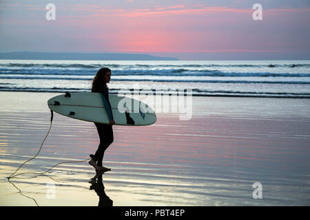 Giovani femmine surfer portando la sua tavola da surf come lei teste fuori in mare per la cattura di un'onda surf a Condino Spiaggia, North Devon, Inghilterra, l'Europa. Foto Stock