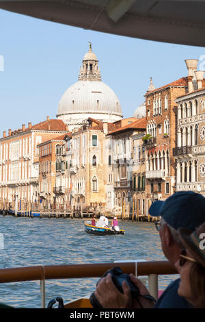 In viaggio con il vaporetto pubblico trasporto Grand Canal, Venezia, Veneto, Italia in prima persona POV della Basilica di Santa Maria della Salute con turiste Foto Stock