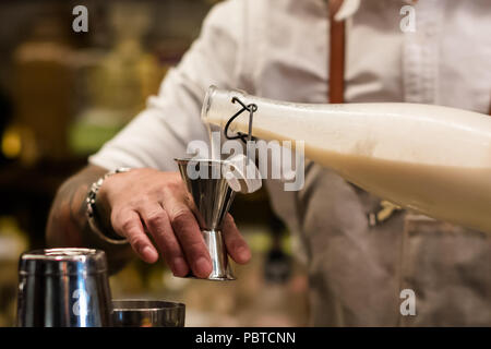 Professional Bartender versando cocktail ingrediente dalla bottiglia di jigger. Barman tenendo in mano destra cocktail attrezzo. La miscelazione di processo di bevanda. Foto Stock