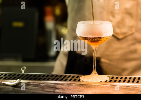 Professional Bartender versando cocktail da shaker in vetro. La miscelazione di bevanda alcolica processo. Close up immagine sfocata con una parte del corpo umano. Foto Stock