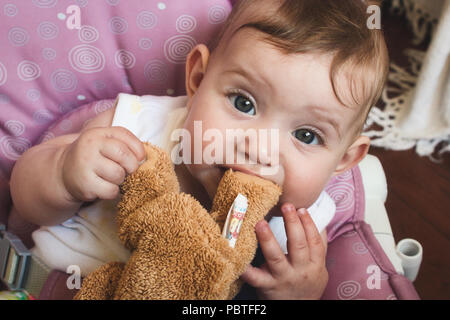 Carino bambina gioca con il suo marrone orsacchiotto di peluche e masticare su orso il piede Foto Stock