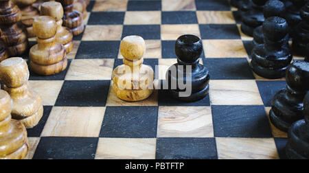 Il vecchio in legno di olivo set di scacchi con scheda staunton pezzi e in bianco e nero di pedine combattendo testa a testa Foto Stock