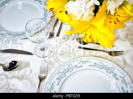 Elegante set da pranzo per un pasto romantico su una tovaglia bianca in un lussuoso ristorante con bouquet di fiori in un vaso sul tavolo Foto Stock