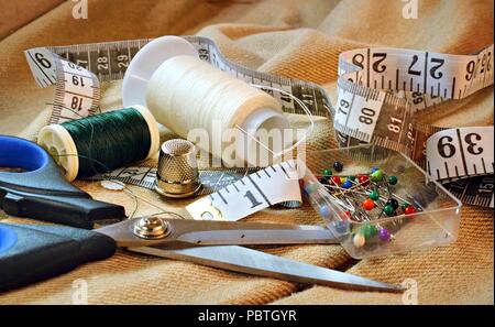 Vista dettagliata del kit di cucitura su sfondo di tessuto comprese le forbici, bobine di filo, nastro di misurazione, ditale e spine Foto Stock