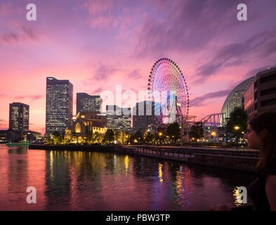 Una vista di una brillante tramonto sulla skyline di Yokohama a Minato-Mirai e il Cosmo orologio 21 ruota panoramica Ferris, come si vede da Unga Park. Yokohama, Giappone. Foto Stock