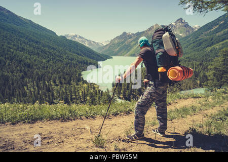 Foto dal retro del turista uomo con bastoni da passeggio con le mani in alto sulla collina vicino lago. azienda turistica di bastoni per Nordic walking Foto Stock