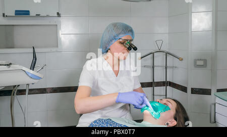 Donna al dentista clinica riceve il trattamento dentale per riempire una cavità di un dente. Restauro dentale e materiale composito la polimerizzazione con luce UV e laser. Foto Stock